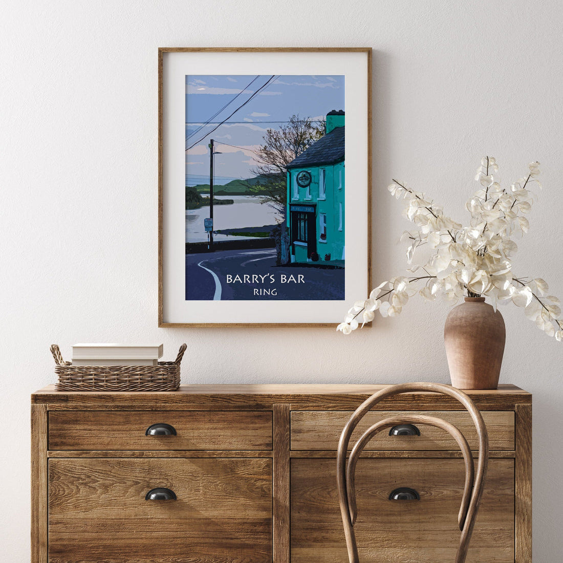 Framed artwork on a wall above a wooden dresser with a chair and vase.