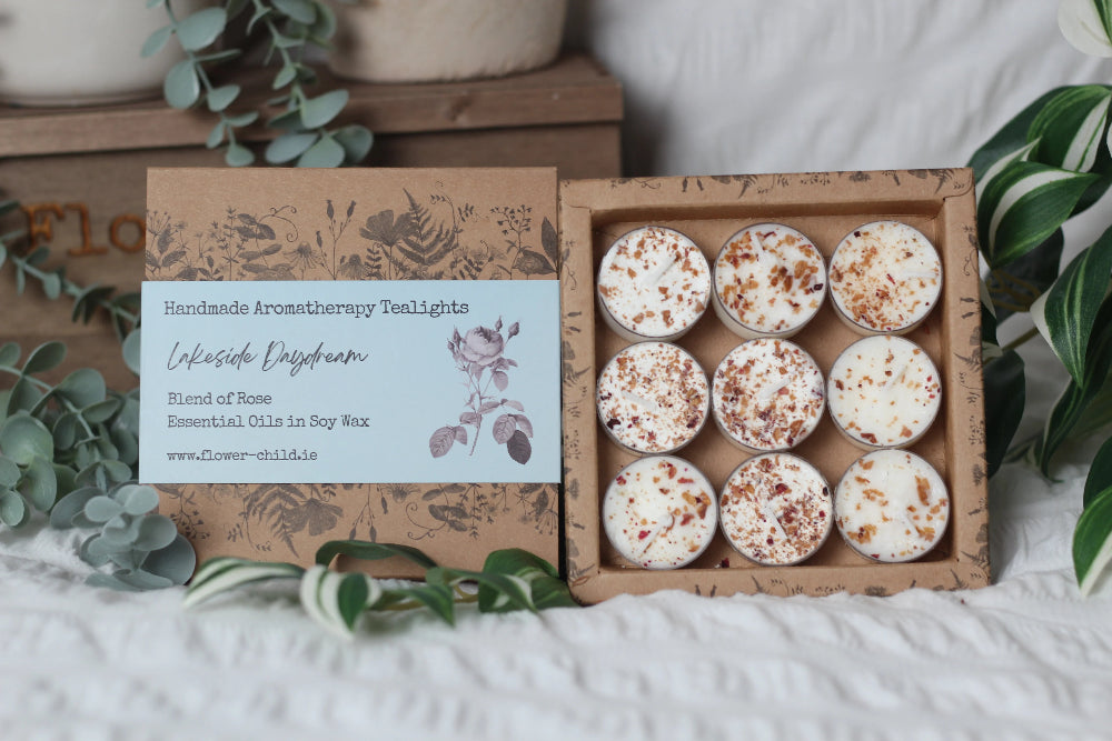 Box of handcrafted aromatherapy tealights with a label on a white surface with greenery.