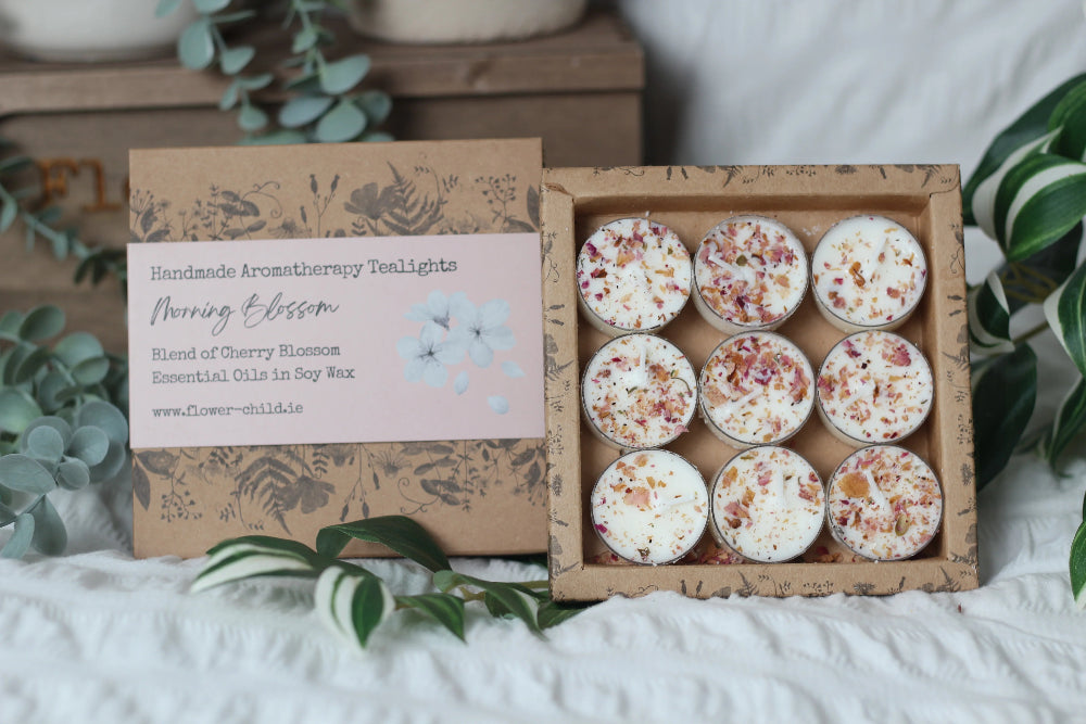 Box of handmade aromatherapy tealights with a decorative label on a white surface with greenery.