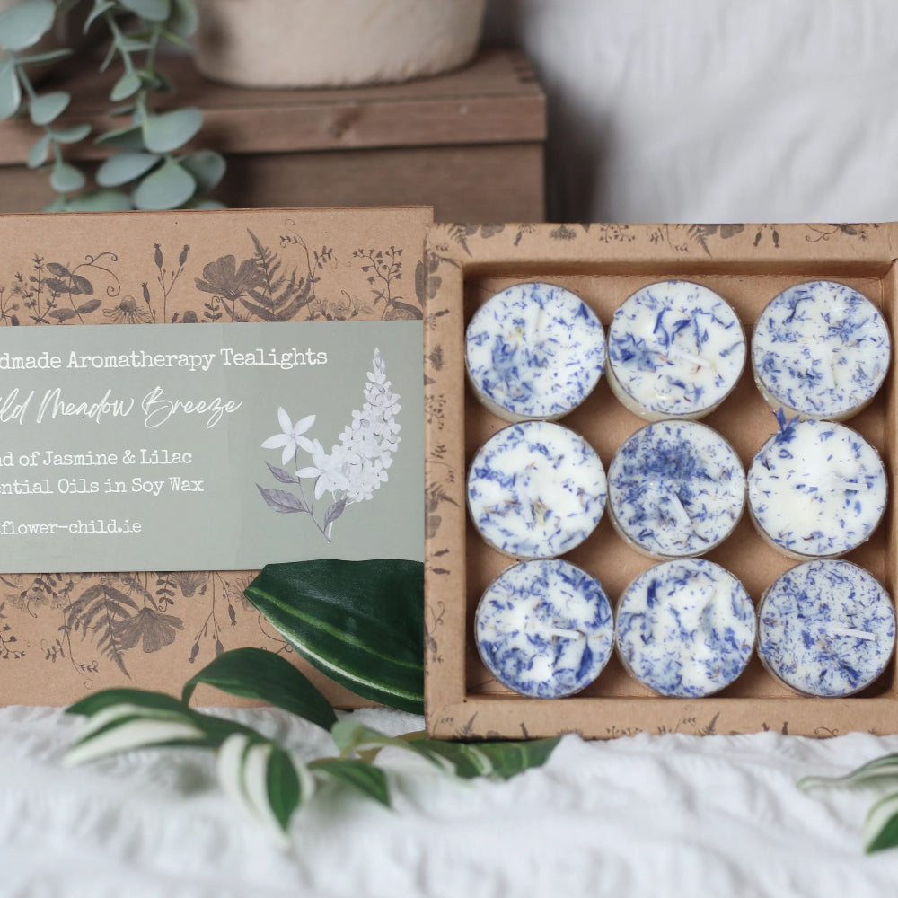 Box of tea light candles with decorative packaging on a white surface with greenery.