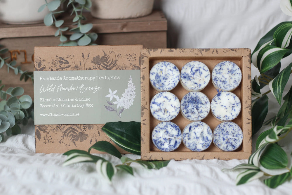 Box of tea light candles with decorative packaging on a white surface with greenery.