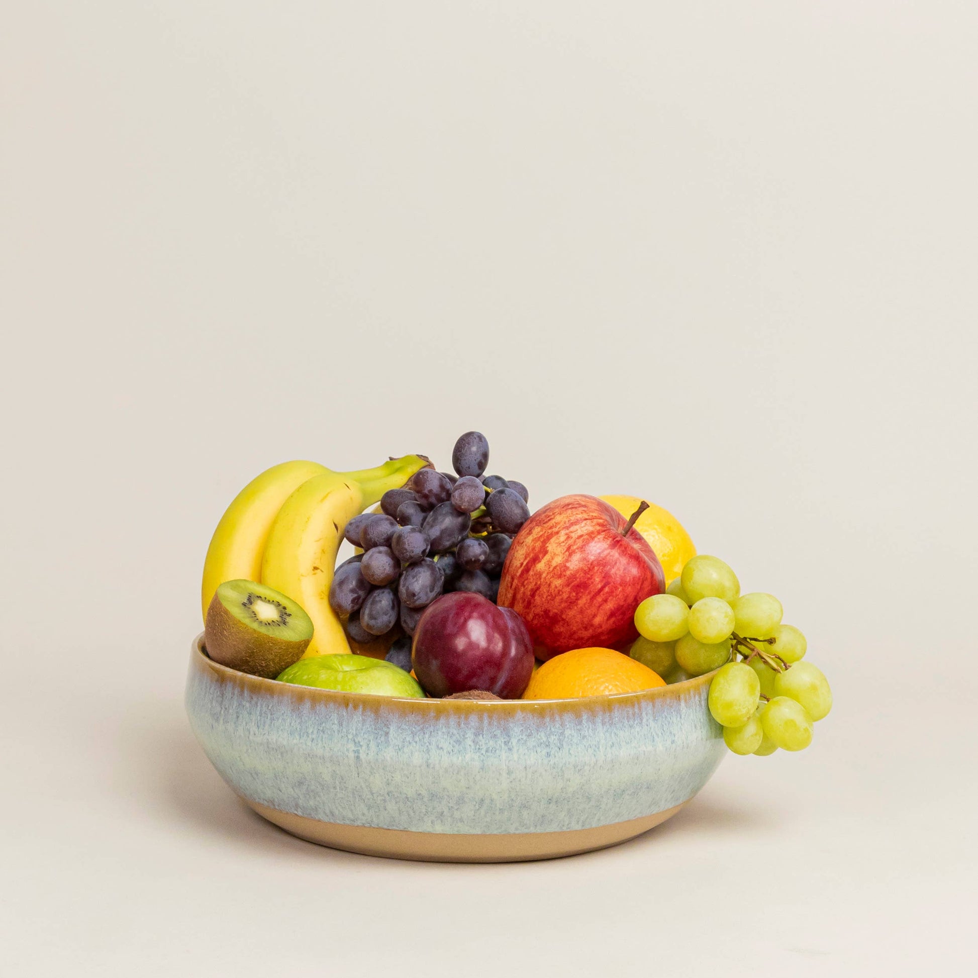Fruit bowl with bananas, grapes, apples, and kiwis on a beige background