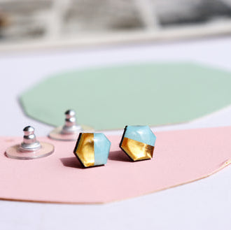 Pair of geometric earrings on a pink and white surface with a green abstract shape in the background.