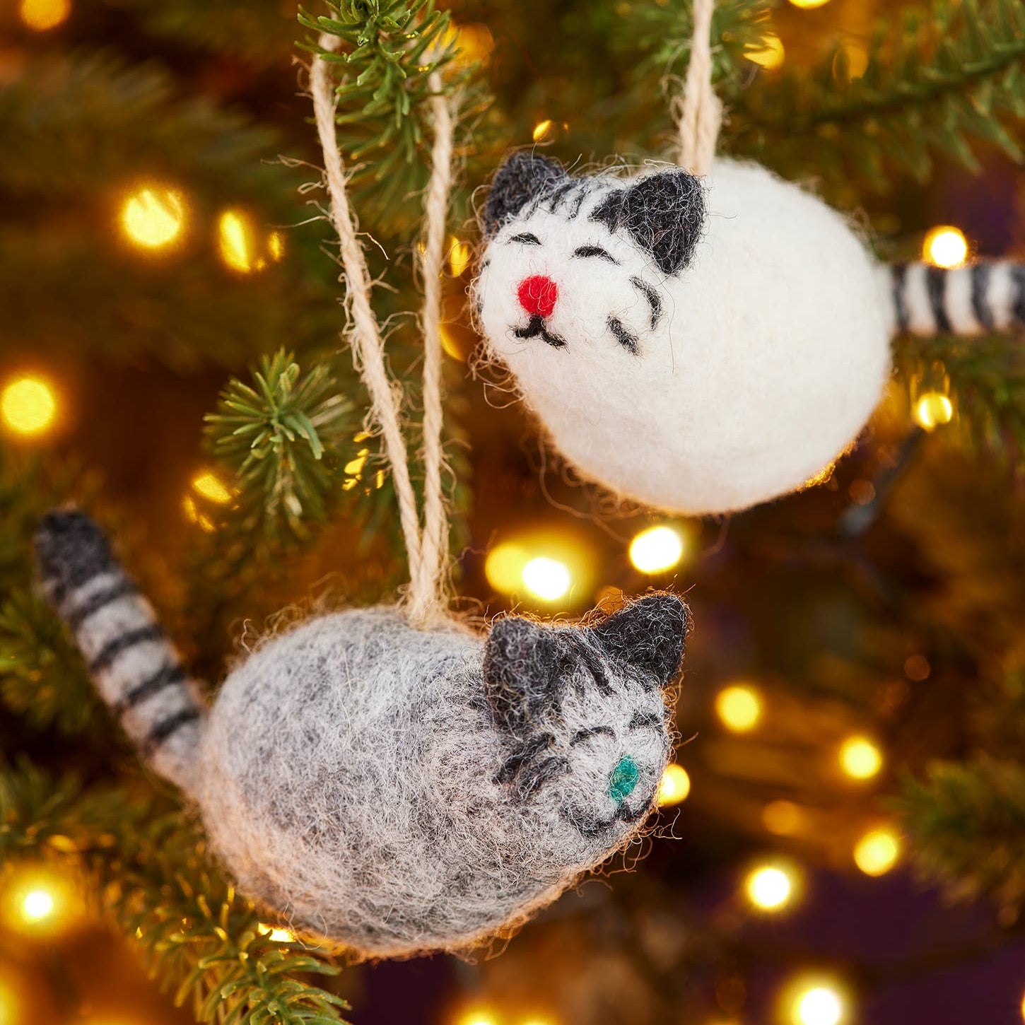 Cat-themed Christmas ornaments hanging on a decorated tree with lights.