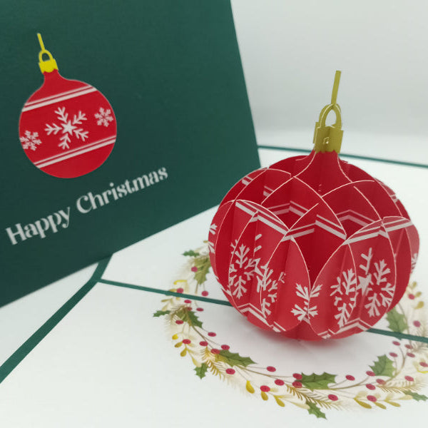 Red Christmas ball ornament with white patterns on a green card with 'Happy Christmas' text.