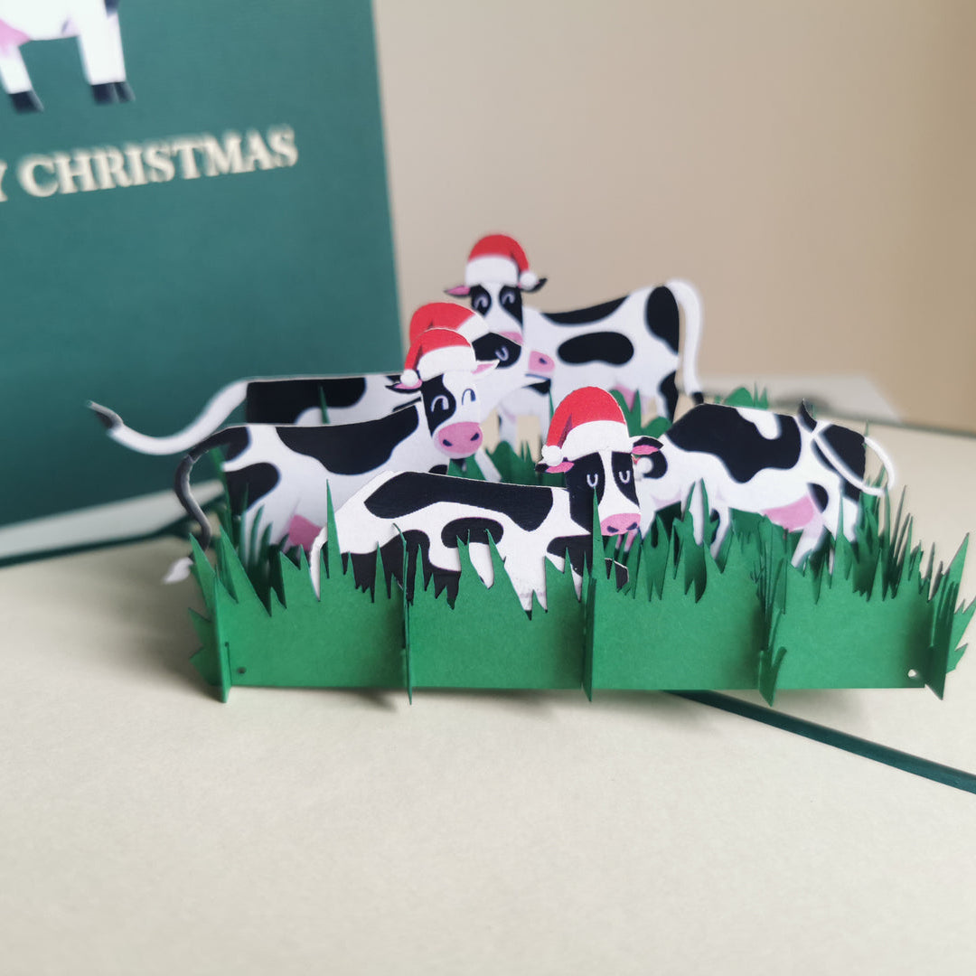 3D pop-up card with cows and Santa hats on a green background