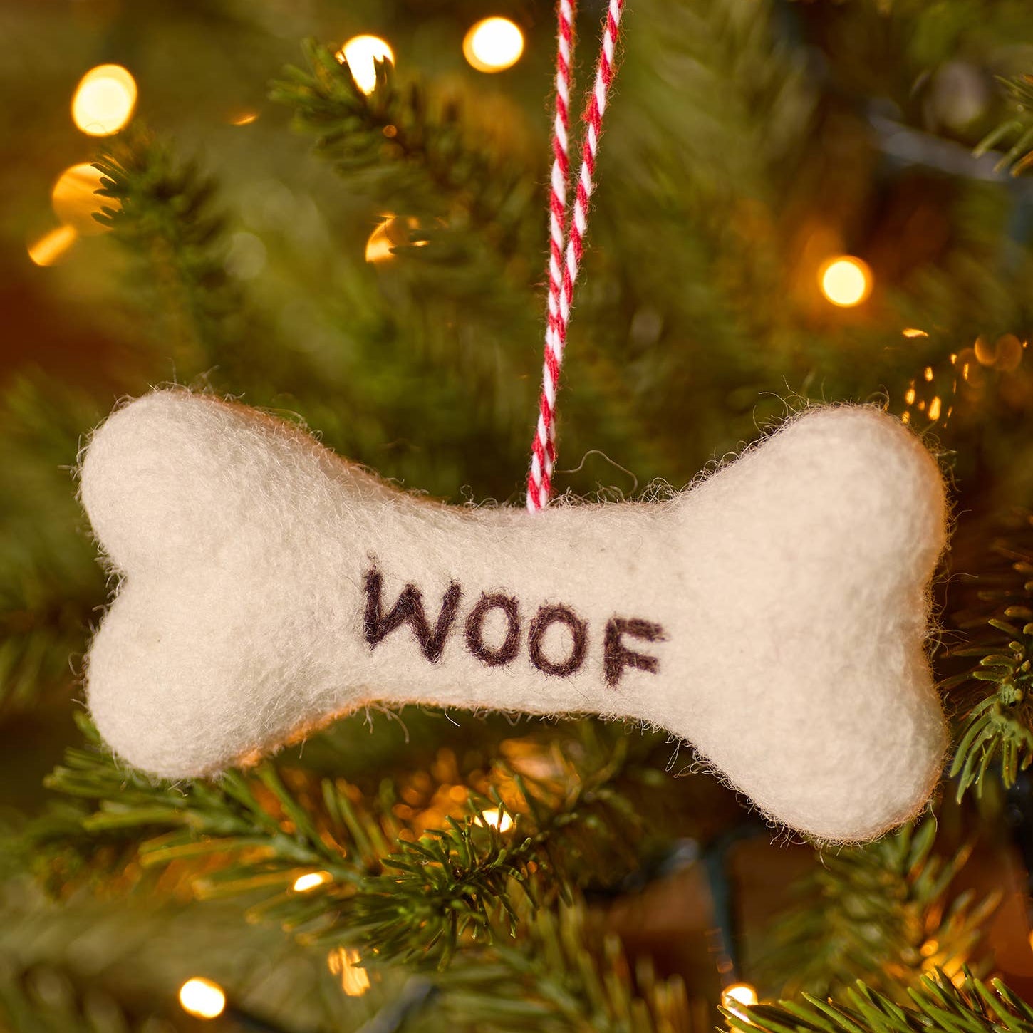 Dog bone ornament with 'WOOF' text hanging on a Christmas tree.