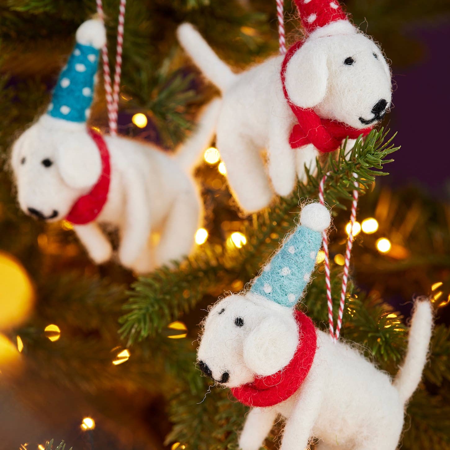 Decorative white dog ornaments with colorful hats and scarves on a Christmas tree.