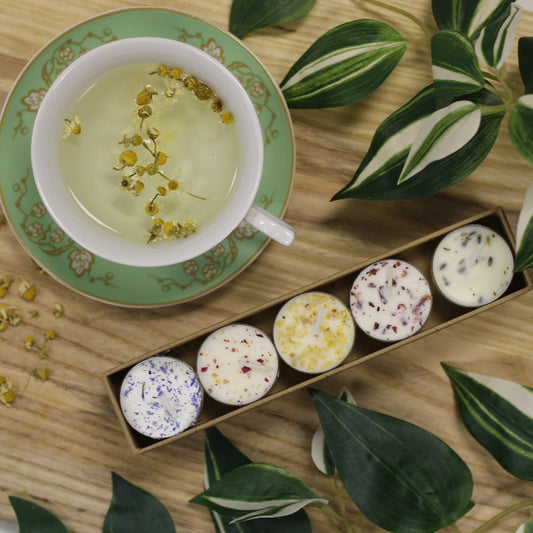 Tea cup with green leaves, a box of candles, and plants on a wooden surface