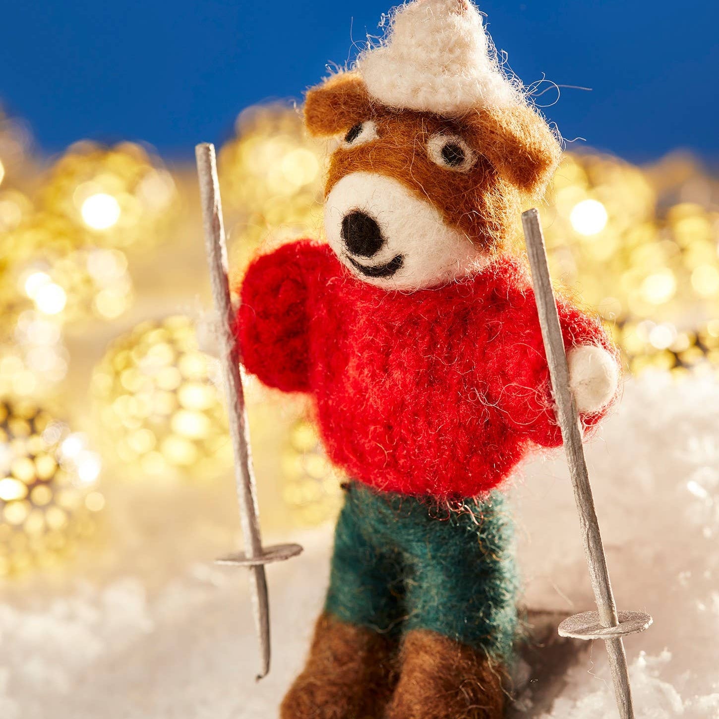 Knitted teddy bear skiing with skis and ski poles against a blurred snowy background