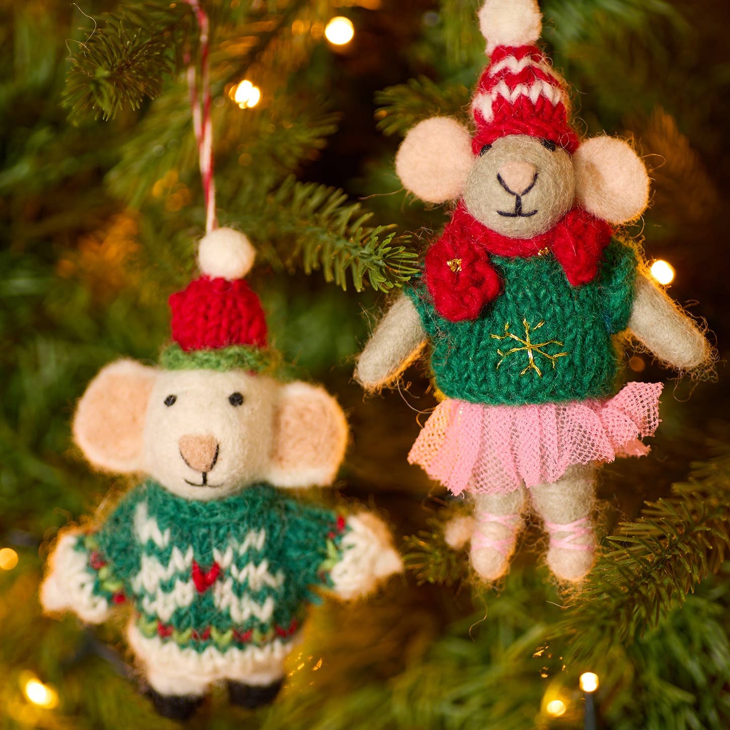 Two knitted mouse ornaments in sweaters hanging on a Christmas tree.