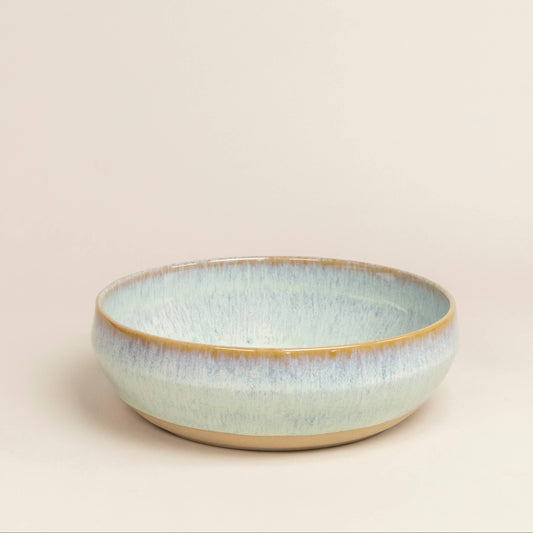 Ceramic bowl with a light blue glaze on a beige background